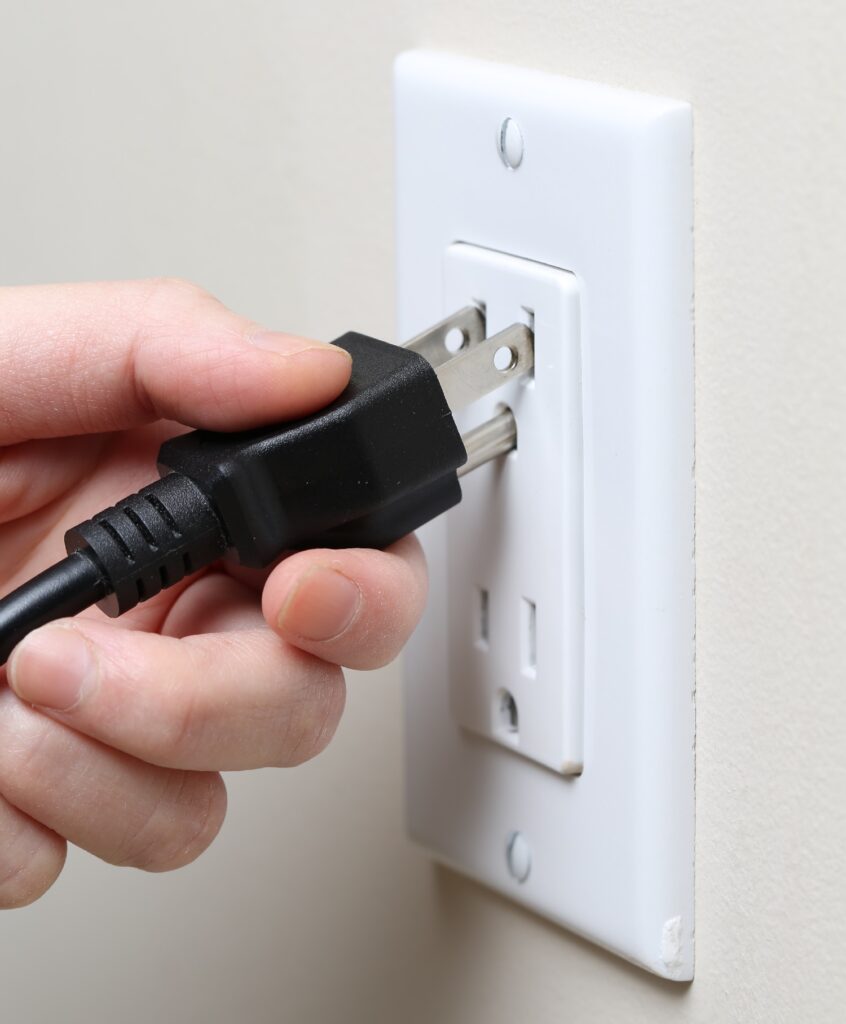 Closeup of a woman's hand inserting an electrical plug into a wall socket