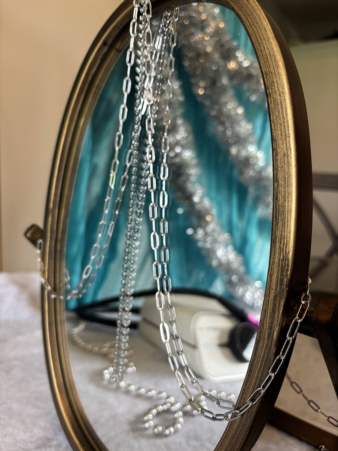 permanent jewelry chains draped over a mirror